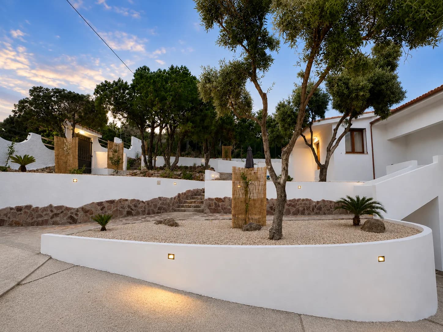 Villa Nina bei blauer Stunde — beide Apartments mit beleuchteten Terrassenmauern und Olivenbaum
